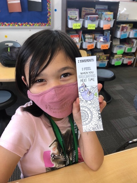 girl wearing a pink holding up a bookmark of a sloth
